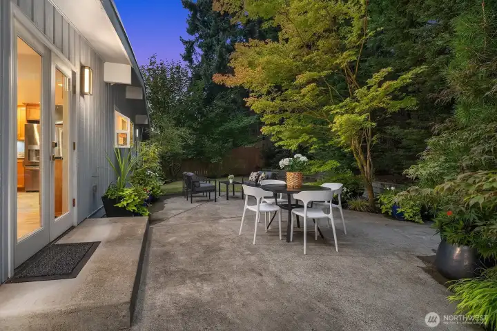 As dusk settles, the private backyard transforms into a magical outdoor retreat, with warm interior light spilling onto the spacious patio, framed by lush mature trees and landscaping for ultimate privacy and tranquility.