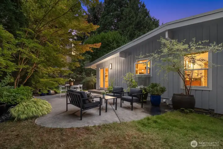 Glowing with warm evening light, this inviting backyard patio with cozy seating and lush surrounding greenery creates an enchanting outdoor living space, perfect for relaxed gatherings or quiet evenings in your own private oasis.
