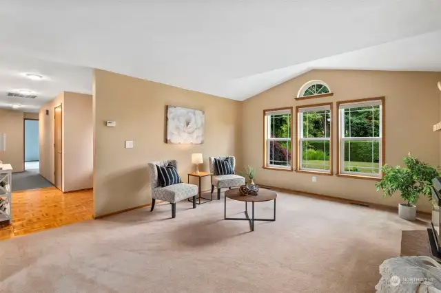 Lovely windows with vaulted ceiling feature the landscaping out front in this living room off the entry.