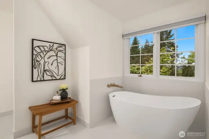 Freestanding soaking tub positioned beneath a bright window retreat.