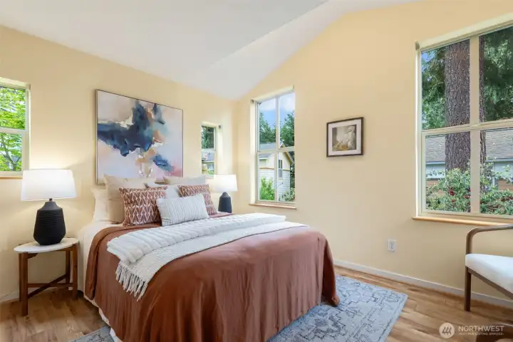 Primary bedroom with vaulted ceilings and lush nature views out of all windows.