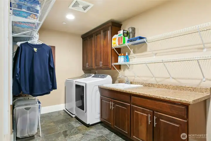 Large laundry room with utility sink, custom built-in cabinets, and generous counter space for folding   and organization.