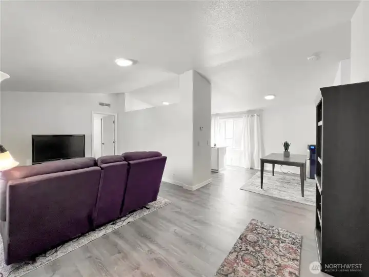 This living room is spacious, open, and bright, featuring vaulted ceilings and durable LVP flooring for a modern, low-maintenance aesthetic. This living room is spacious, open, and bright, featuring vaulted ceilings and durable LVP flooring for a modern, low-maintenance aesthetic.
