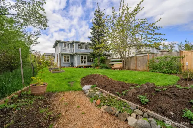 Spacious fenced backyard has gardening space, raised beds, fruit trees and green space on one side to create a secluded atmosphere
