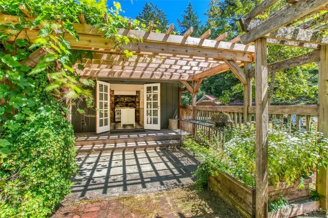 French doors open from the kitchen to a sunny patio with a grapevine-covered pergola —perfect for outdoor meals or relaxing in the shade.