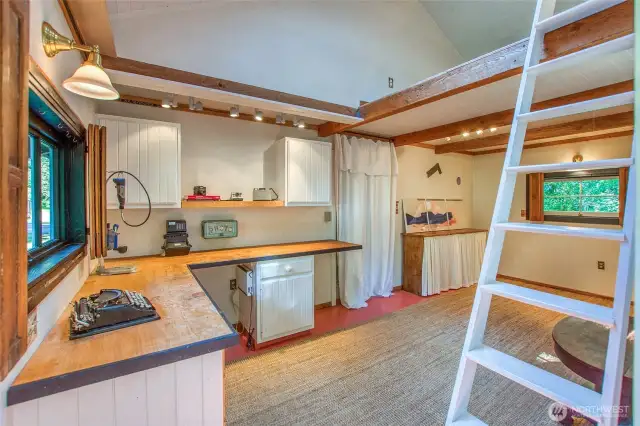 Studio is tucked behind the shop, featuring exposed beams, built-in workspaces, loft access, and windows overlooking the natural surroundings.
