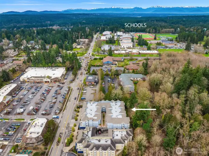 Aerial perspective showcasing the condo’s central Bainbridge Island location near schools, everyday shopping, and Winslow amenities, with surrounding greenbelt adding a sense of privacy and natural beauty.