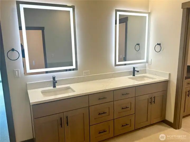 Primary Suite bath has a wide double vanity with quartz counters and backlit mirrors.