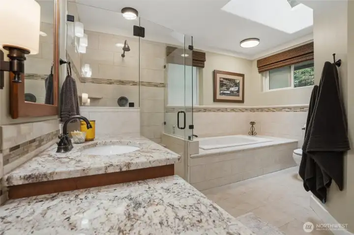 A large, tiled walk-in shower and jacuzzi tub in the primary bathroom enjoys natural lighting from the skylight above.