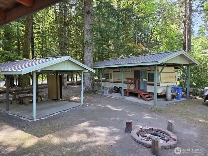 covered picnic shelter with cement floor, fire pit, and travel trailer with toliet plumbed into the septic tank