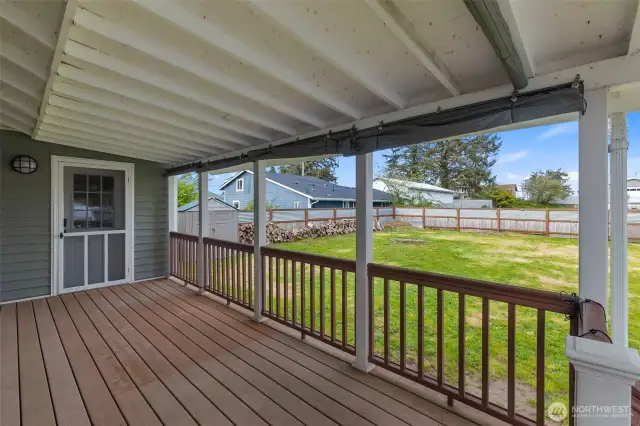 View of  covered back patio  with trek deck. Door allows entrance to primary bedroom. Entire backyard is fenced and has small shed to the left.