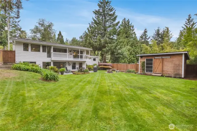 Back of home and fully fenced flat backyard with sprinkler system, raised garden beds, patio, wood fire ring, gas fire pit and garden shed.