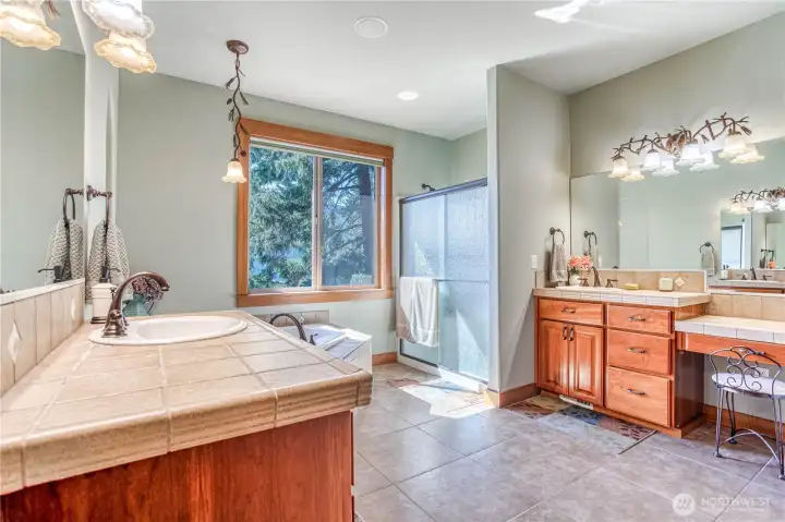 Primary bathroom suite has dual sinks, ceramic tile counters, make up area, large soaking tub, separate shower, & a view of the lake!