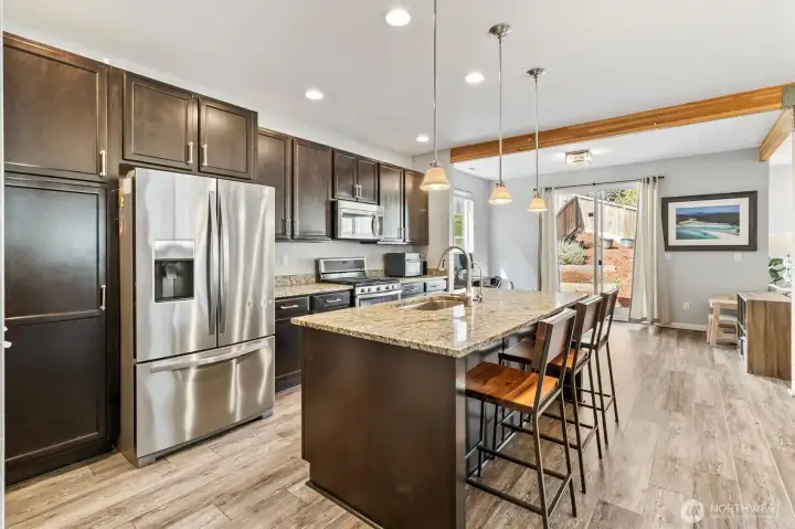 Kitchen with granite countertops, large island seating, stainless steel appliances, and adjacent dining space.