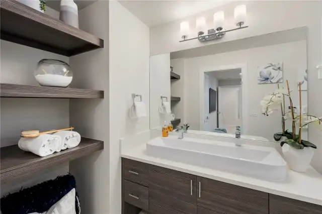 Picture of previous model home primary bathroom.  All home feature primary bathrooms with tiled showers and floors, dual sinks, and built in storage alongside modern cabinetry.