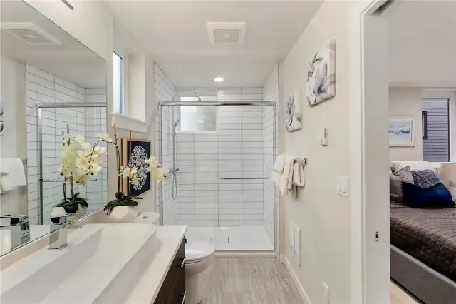 Picture of previous model home primary bathroom.  All home feature primary bathrooms with tiled showers and floors, dual sinks, and built in storage alongside modern cabinetry.