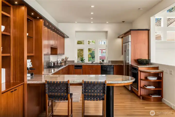 A breakfast bar with a marble top extends out from this beautifully designed kitchen with an oversized sub-zero fridge to the right.