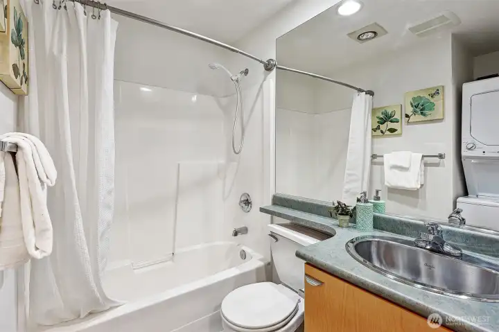 Bath is clean and modern, including tub surround and washer/dryer unit.