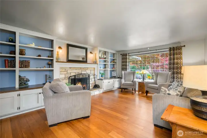 Cozy living room with wood burning fireplace, custom built shelving, and laminate hardwood flooring.