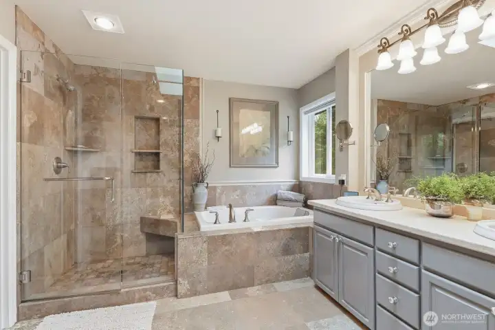 The remodeled primary ensuite bathroom offers premium finishes and thoughtful design. Travertine marble flooring creates an elegant foundation, while the beautifully tiled walk-in shower features a seamless glass enclosure and sophisticated detailing.