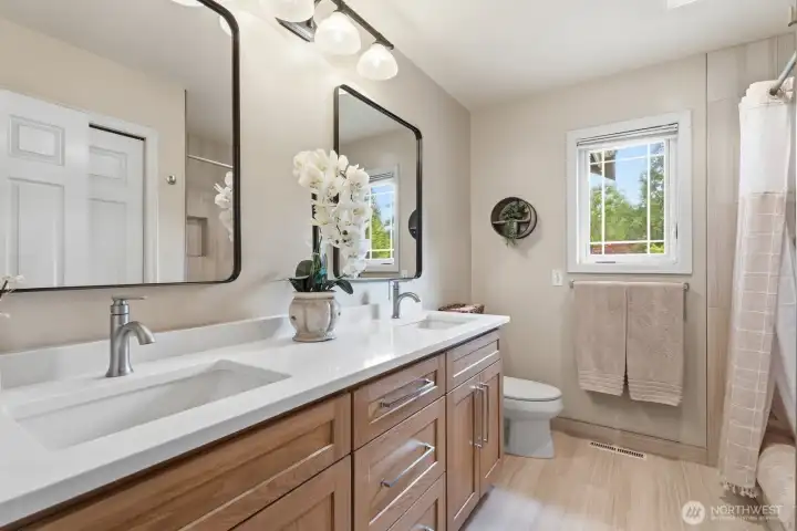 Recently updated hall bathroom featuring designer tile flooring, a beautifully tiled tub/shower surround, a new quartz vanity and stylish portrait mirrors.