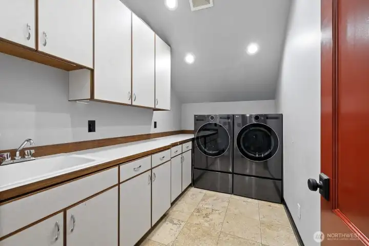 An upstairs laundry facility conveniently located near bedrooms and bathrooms is a modern solution designed to simplify household chores and offer convenience to the household by eliminating the need to carry heavy loads of laundry up and down stairs, thereby enhancing efficiency and comfort in daily routines.  The newer washer and dryer units are high-efficiency and designed to save water and energy while providing powerful cleaning performance.  Overhead cabinets provide additional storage space for laundry supplies and accessories.  Countertops offer a convenient spot for folding garments and sorting laundry.  The utility sink is perfect for soaking stained items or hand-washing delicate fabrics.  This upstairs laundry facility is a valued addition to this stunning home.