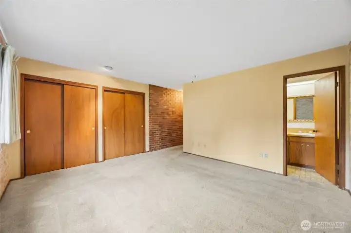 Wall of closets in the primary suite. Like true 70s homes, this one has so much storage everywhere you turn! Brick accent wall in this room as well. En suite bathroom shown to the right.