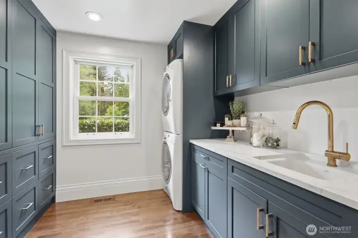 The large laundry room also outfitted with walls of custom cabinets, built-in laundry sorting bins, utility sink and quartz counter. The large laundry room also outfitted with walls of custom cabinets, built-in laundry sorting bins, utility sink and quartz counter.