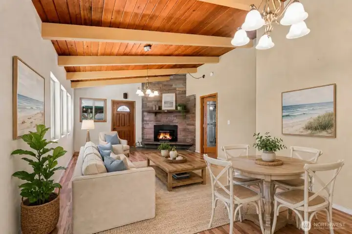 Light-filled living room with a warm wood-plank ceiling, cozy pellet stove, expansive windows, and flexible space for dining, and relaxing. (Virtually Staged) Light-filled living room with a warm wood-plank ceiling, cozy pellet stove, expansive windows, and flexible space for dining, and relaxing. (Virtually Staged)