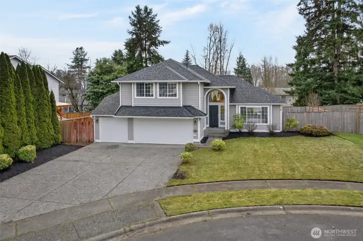 The home sits in a quiet, residential setting with a broad driveway and an attached two car garage that makes daily life easy. Mature evergreens and fencing add a sense of separation, giving you comfortable outdoor space without heavy maintenance.