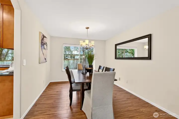 The dining room is positioned for effortless hosting with a direct connection to the kitchen and a window that brings in soft natural light. Wood toned flooring adds warmth and continuity as the spaces flow together.