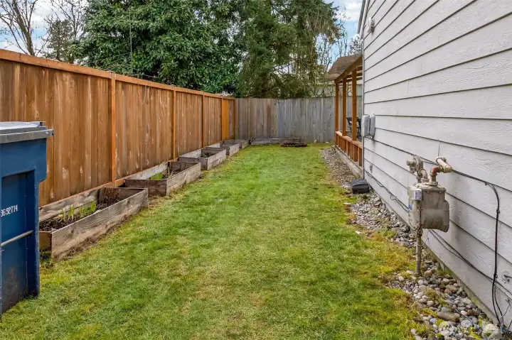 A fenced side yard creates useful outdoor space with raised garden beds ready for herbs, flowers, or seasonal planting. The level lawn strip is easy to maintain and offers a convenient path between the front and backyard.