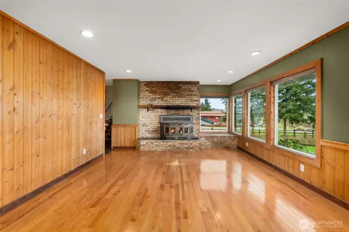 A warm and inviting living room featuring beautiful hardwood floors, warm real wood plank walls and a classic fireplace with insert that creates a focal point for your decorating and beautiful views over the back yard.