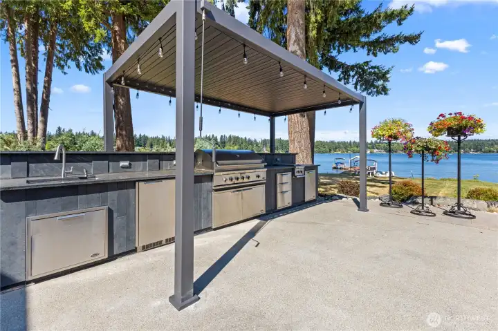 Outdoor covered kitchen with built in appliances including sink, mini refrigerator, BBQ grill, two burner stove and granite countertops