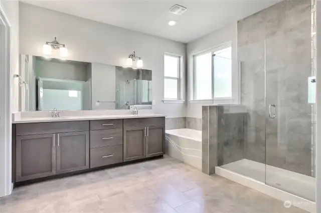 This luxurious primary bathroom features double sinks with sleek quartz counters and backsplash, elegant tiled floors, a spacious soaking tub, and an oversized stand-up shower with stunning tile details. A beautifully designed space, perfect for unwinding in style and comfort.