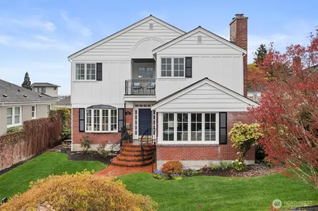 This custom built home blends traditional charm with tailored sophistication. The façade features a striking mix of red brick and crisp white siding, accented by black shutters and iron railings. A curved brick walkway and steps lead to the covered entry, setting a gracious tone from the moment you arrive.    Symmetrical gables, a Juliet balcony, and divided-light windows—part of a custom Marvin wood-clad package—highlight the home's architectural integrity. Surrounded by lush landscaping and mature trees, the exterior is as refined as it is welcoming.