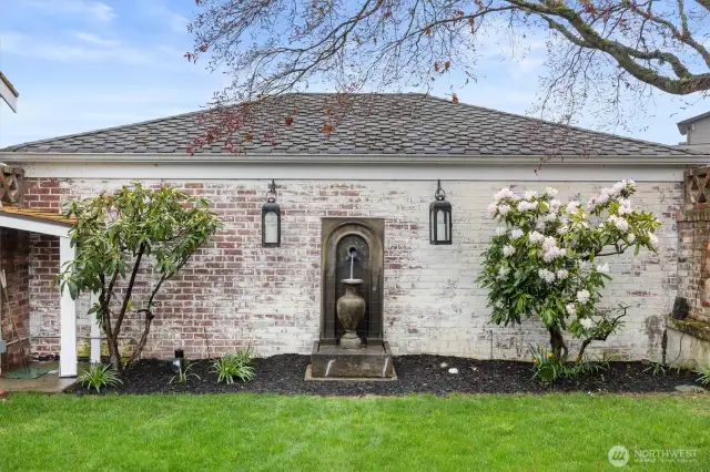 A vintage-inspired fountain set against a whitewashed brick wall adds the calming sound of water and architectural interest. Lantern lighting completes this sophisticated and serene retreat—tailored for relaxed gatherings and quiet moments alike.