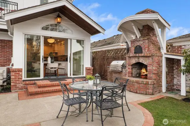 A Carson wall sconce from Rejuvenation illuminates the sleek black soapstone slab countertop, where a built-in 38” Delta Heat gas grill with rotisserie awaits. Positioned beside a custom brick outdoor fireplace and framed by a hand-built brick privacy wall, this outdoor kitchen blends function and craftsmanship—perfect for year-round entertaining.