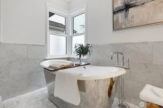 Free standing Bathtub with Polished Stainless Exterior reflects the marble mosaic tile finished with wainscot and a chair-rail.