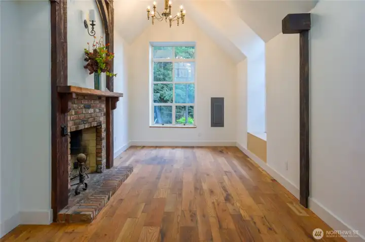 Light-filled living room with vaulted ceilings, rustic brick fireplace, and a picture window overlooking the garden—complete with a cozy window seat for the perfect reading nook.
