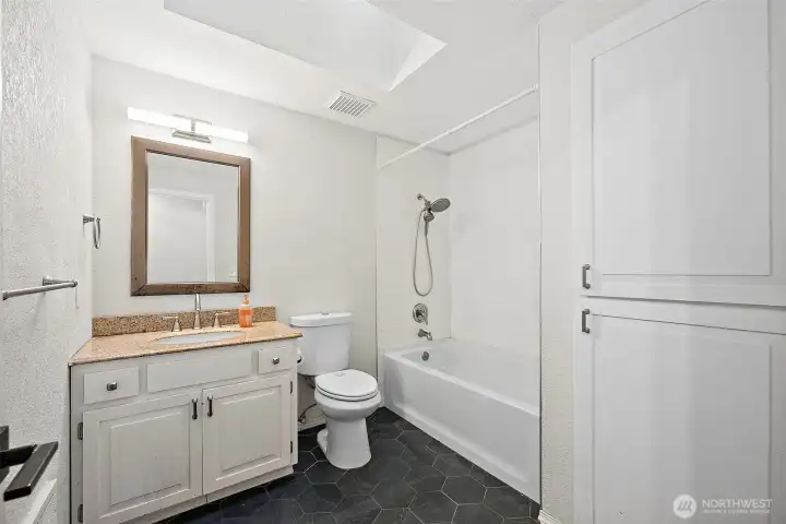 Black hexagon tile floor in full bathroom with storage cabinets inset into wall. Skylights bringing in extra light.