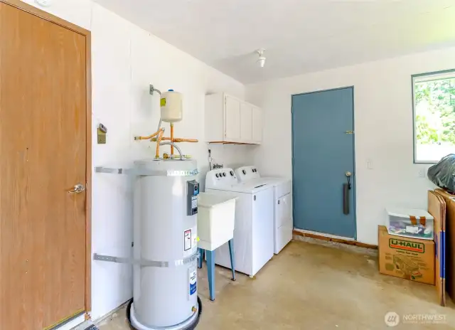Garage with new electric water heater - just installed in December, 2024. Also washer and dryer along with utility sink and cupboards are here in the attached garage, along with an EV charging outlet!