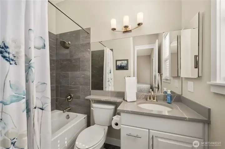 Guest bath offers Quartz counters, tile flooring and tile surround tub and shower.