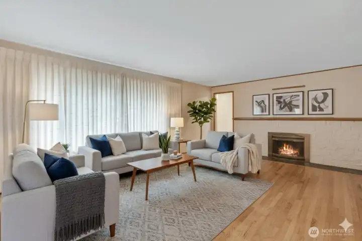 Generous living room featuring hardwood floors, fireplace and large picture window pouring natural light into the room.