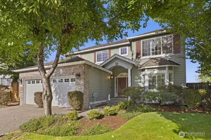 Charming curb appeal with mature landscaping, brick accents, and a welcoming covered entry.
