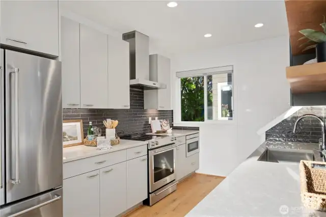 Beautifully designed kitchen features SS KitchenAid appliances, tile backsplash, under mount lighting, custom floating shelves, quartz counters and space to cook up a delicious meal for guests.