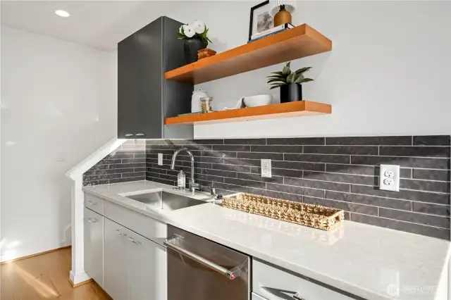 Beautifully designed kitchen features SS KitchenAid appliances, tile backsplash, under mount lighting, custom floating shelves, quartz counters and space to cook up a delicious meal for guests.