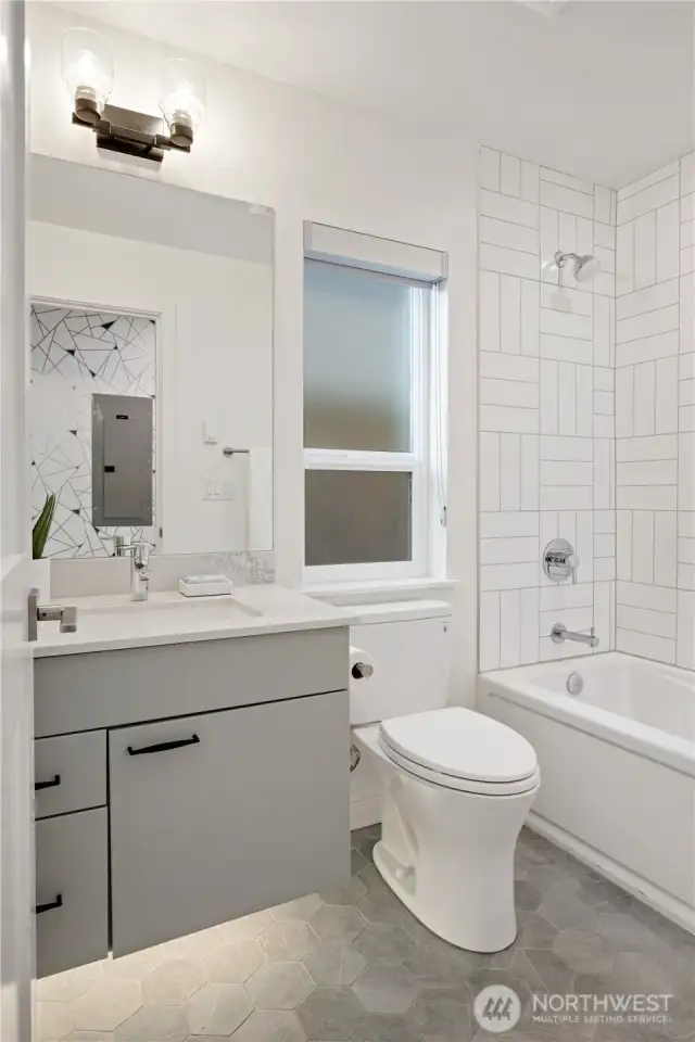 Entry level guest bathroom with hexagon tile heated floors, floating vanity with under mount accent lighting, and full tile surround with bathtub.