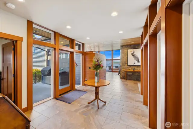 View of entry looking towards the living space and out to the water. Covered entry on one side is balanced by a covered patio space on the other with outdoor kitchen area and built-in BBQ. Both entrances and spaces were designed with multi-generational living or aging in place potential needs with zero steps and wider areas of access.