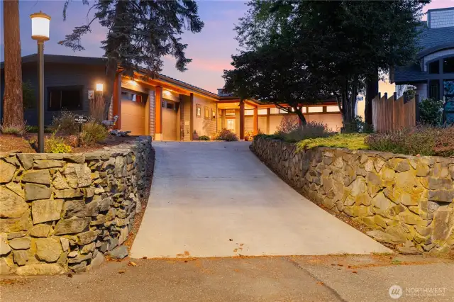 Sunset view of the home from the street with beautiful rock wall work and under lighting.